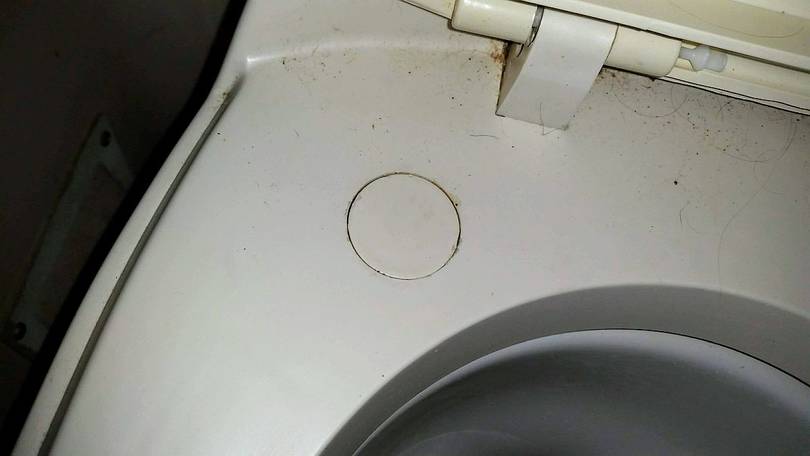 Small round cover over access hole to rear toilet nut on the flange bolt